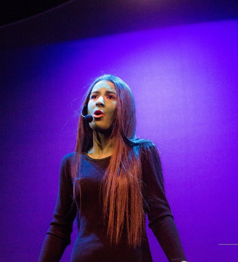A student singing under stage lights